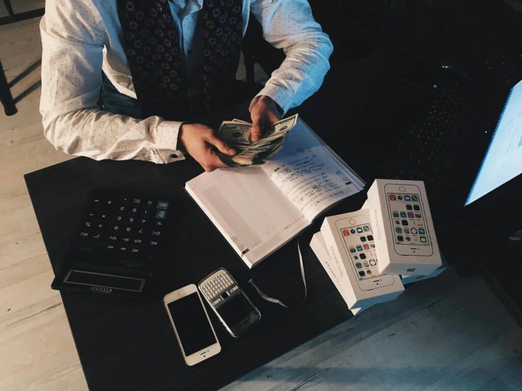 10 Reasons Your Small Business Needs a Bookkeeper And How to Choose One 1 Businessman organizing finances with tech devices and cash on desk.
