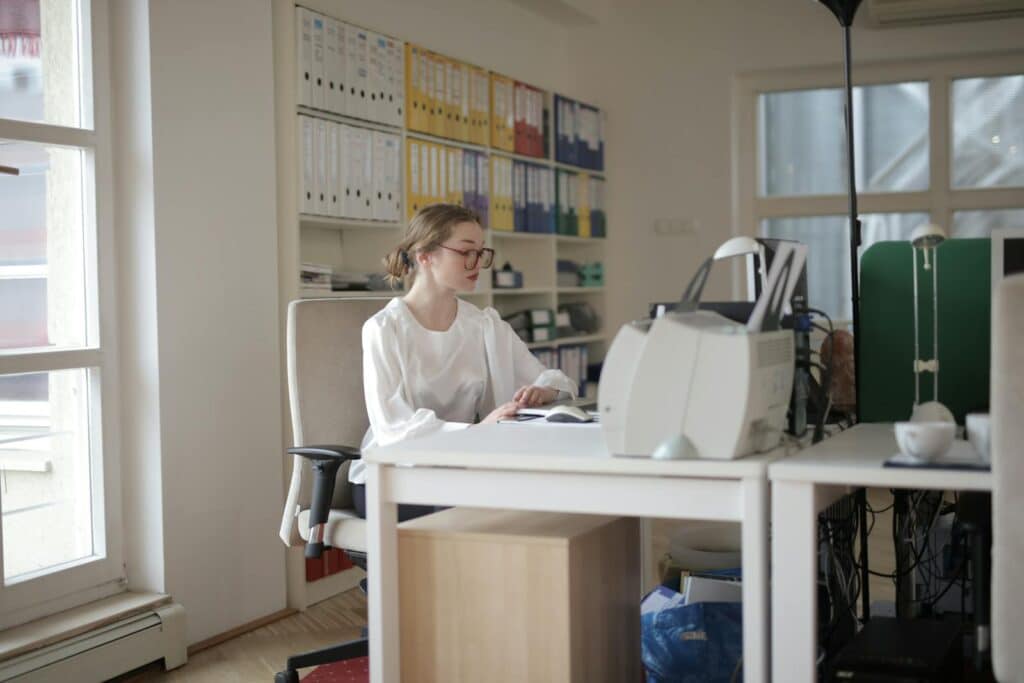 10 Reasons Your Small Business Needs a Bookkeeper And How to Choose One 3 Focused woman working in a modern office filled with files and equipment.