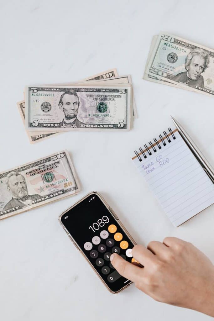How to Calculate Profit: A Simple Guide for Small Business Owners 1 Overhead view of a hand using a calculator with US dollars and notes, representing finance and budgeting.