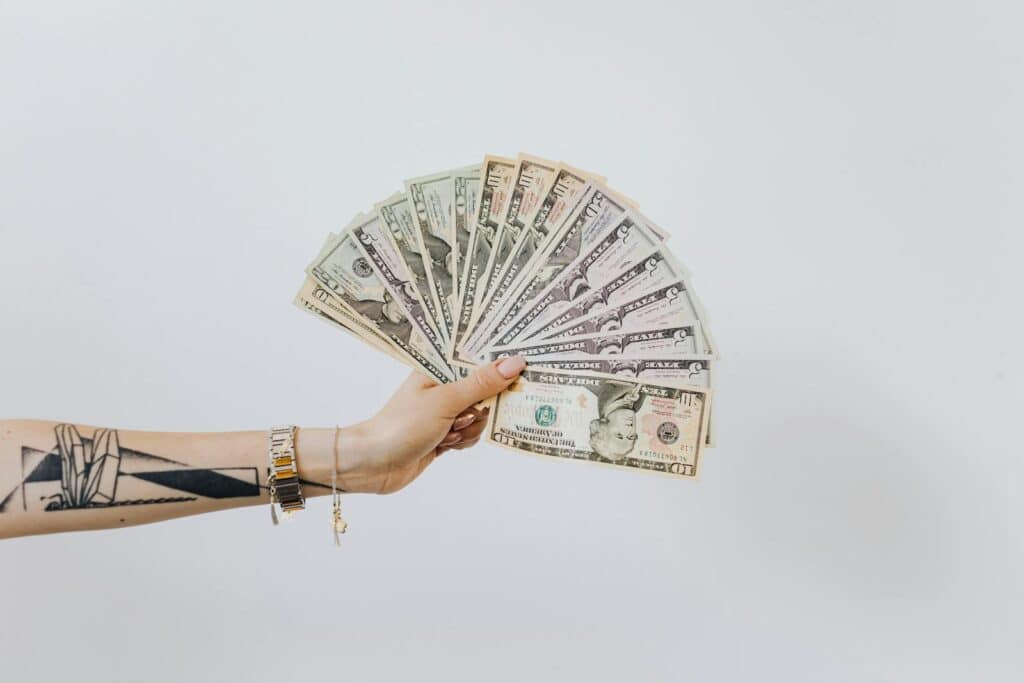 What is Net Profit? Essential Guide to Understanding and Calculation 7 Tattooed arm holding a fan of US dollar bills on a white background, symbolizing wealth and financial success.