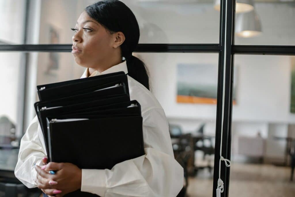 A confident black woman holding files, standing in a modern office environment.